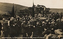 A Salvation Army funeral cortege, with men carrying the coffin. The streets are lined with people, some of whom have Salvation Army banners.