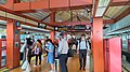 A photograph of Choa Chu Kang station's LRT platform. It consists of red beams which support an inverted 'V' shaped roof. The platform is crowded