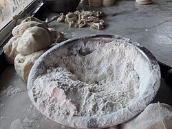 A bowl of white flour next to balls of dough.
