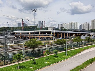 A wide, daytime view of an at-grade train depot showing several parked DTL trains under a semi-open-air structure