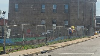 The fence of a park with a thin blue line U.S. flag and flowers in the middle of the fence.