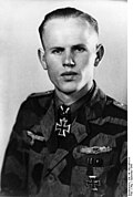 A man wearing a camouflage military uniform with an Iron Cross displayed at the front of his uniform collar.
