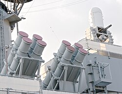 A quartet of grey colored cylindrical canisters positioned roughly in the center of the image, with the canisters pointed at angle with the base to the lower left. Another quartet is positioned on the left of the image. A white cylinder with a dome can be seen on the upper right of the image.
