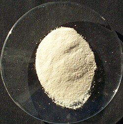 A small colorless saucer holding a pale-yellow powder