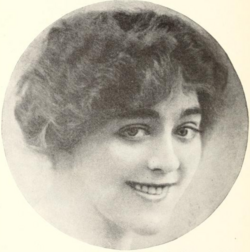 A smiling young white woman with dark wavy hair, in a circle frame