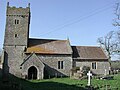 A square stone three step cross base, supporting a socket stone, in front of a small stone church and tower