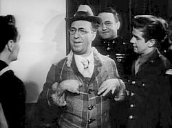 a man in what appears must be a brightly colored suit and hat, as this is a black and white photo, is the centre of attention speaking to three young men