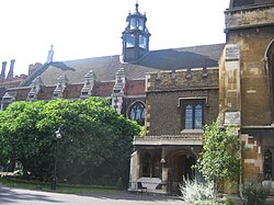  A long, low building of brick and stonework, with arched windows. It is partially obscured by trees and shrubs. The slate roof features a six-sided tower of stone and glass.