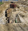 A vibratory pile driver on a steel H-pile (foreground) powered by a diesel engine (background).