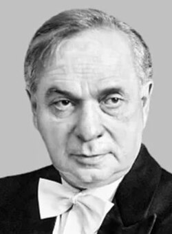 Black and white studio publicity shot of a clean-shaven, elderly, half-smiling man with short, receding, greying hair, with a left parting. He looks askance from under dark brows, one brow being raised, as if to make a point.